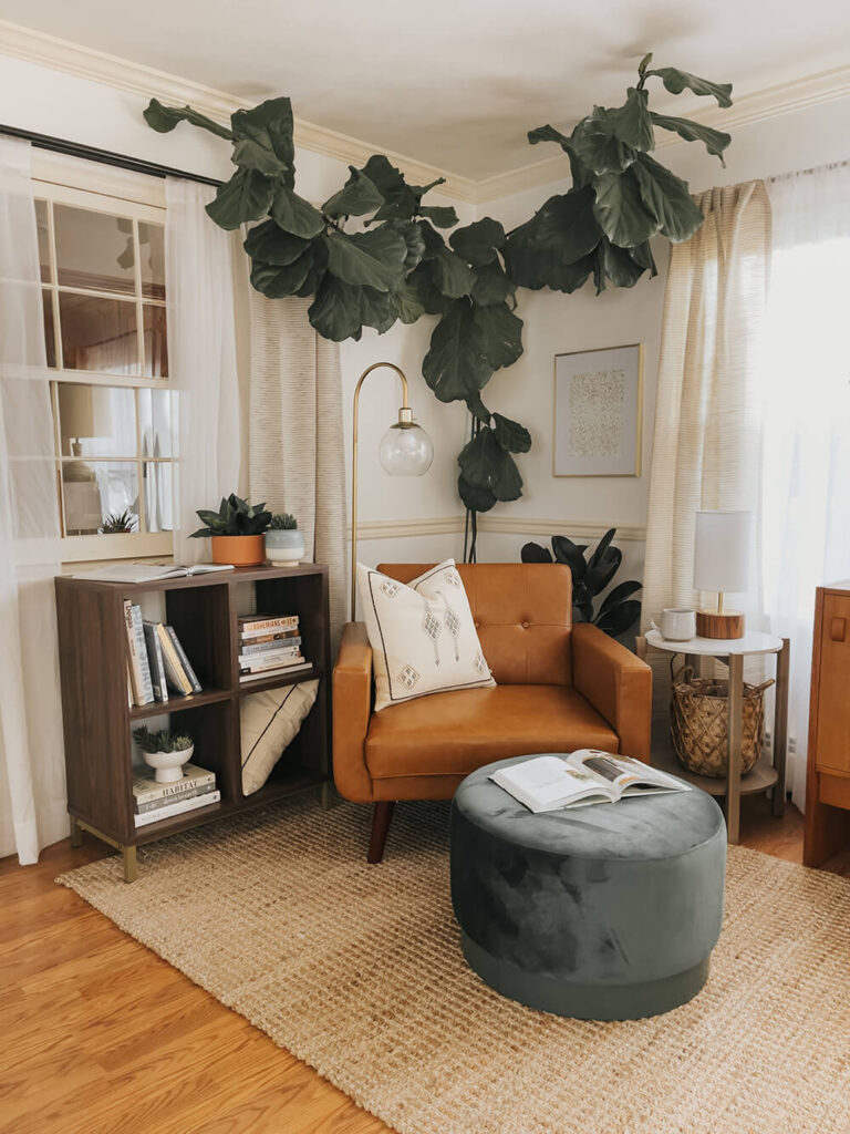 Simple reading nook ideas with a cozy leather chair, ottoman, throw pillow, side table, floor lamp and bookshelves and house plants.