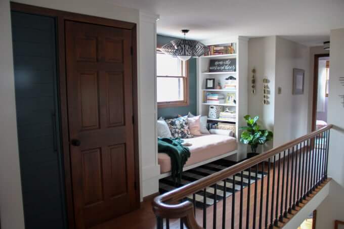 An awkward space at the stop of a stairway is turned into a cozy reading nook with simple Ikea bookshelves and a cushioned platform.
