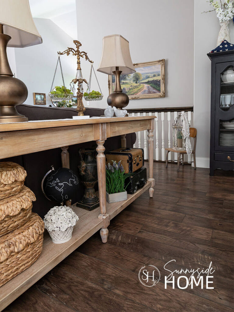 Sofa table decorate for summer with scalloped baskets, crate of flowers, suitcases, and vintage decor with moss.