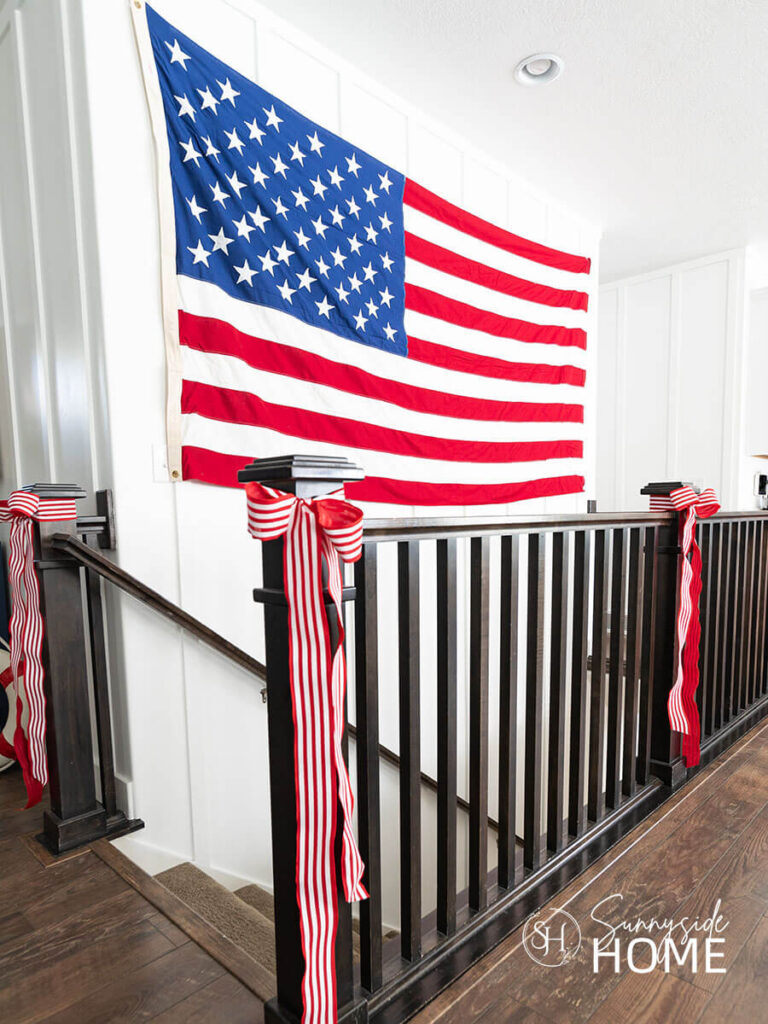Dramatic 4th of July decorating ideas, a large flag is hung on the wall over the stairway.