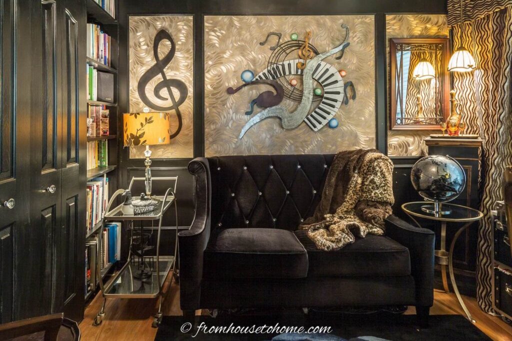 A moody small room is created into a cozy home library with bookshelves, loveseat, bar cart, side table, hanging lamp.