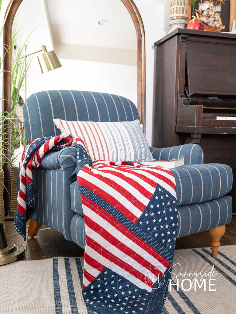 Blue and white striped chair in the living room is styled for the fourth of July with an American flag quilt and a red, white and blue pillow.