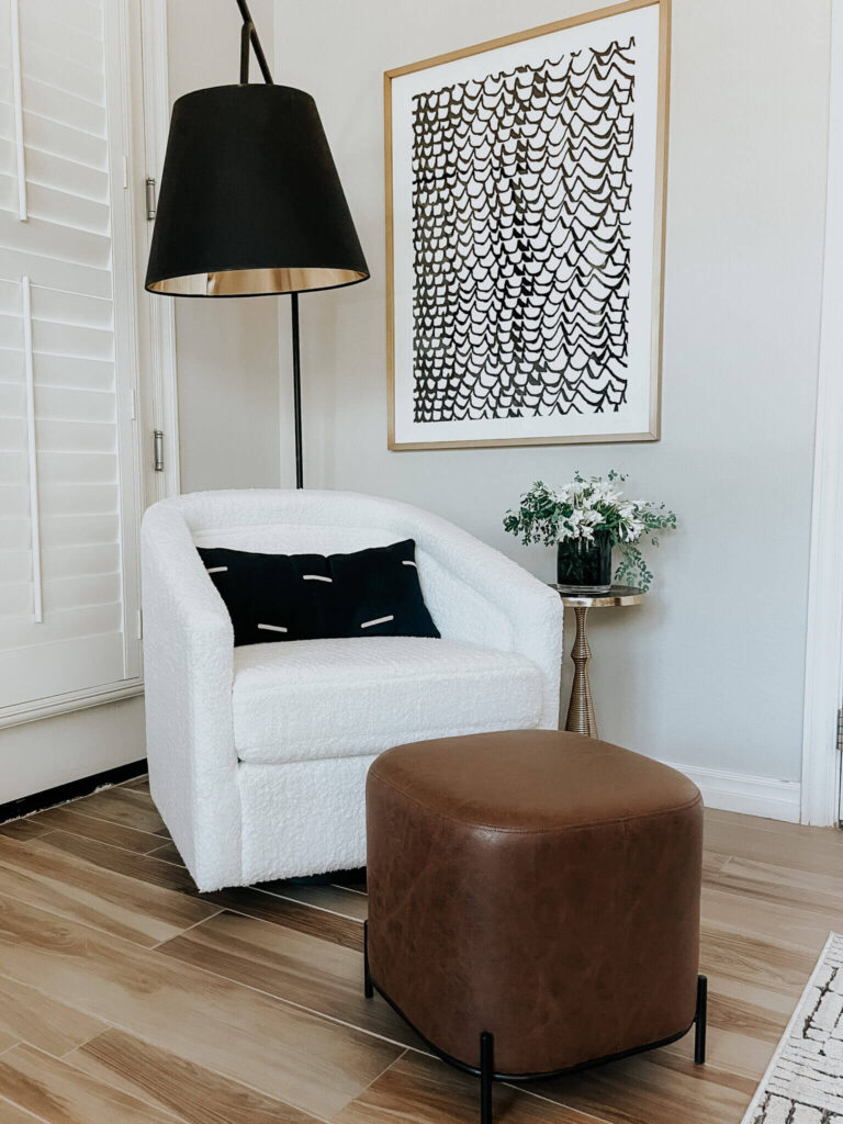 Simple reading nook ideas with a cozy chair, ottoman, throw pillow, side table, floor lamp with black and white wall art.