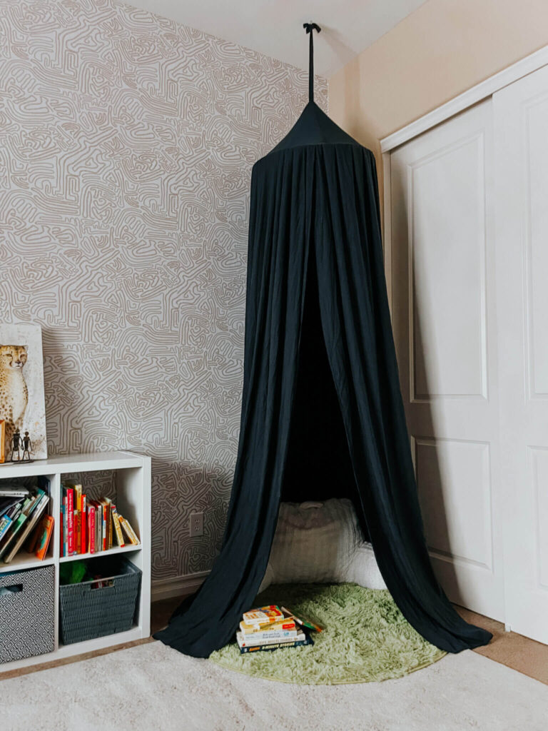 A canopy is hung from the ceiling over a shag rug with a pillow, creating a cozy kids reading nook.