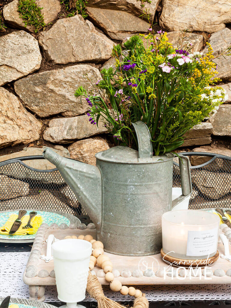 Old galvanized watering can with wildflowers on a patio table.