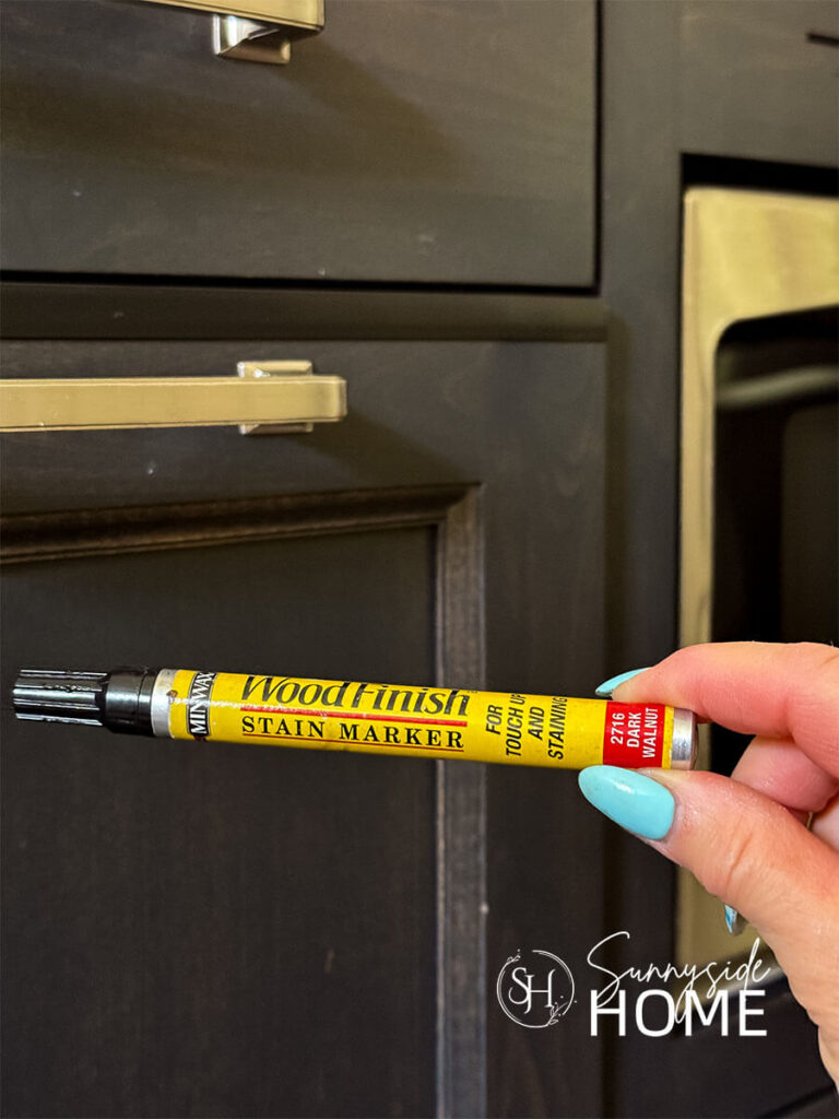 Woman holds a stain marker pen in the color of dark walnut to fix chipped kitchen cabinets.