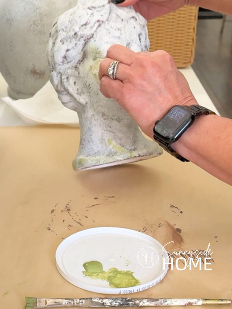 A woman dabs mossy green paint onto a vase with a damp coffee filter.