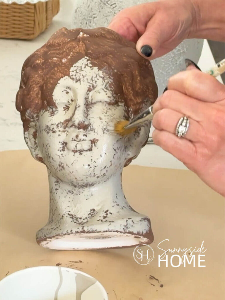 A woman pounces on taupe paint over brown paint to add texture and depth with paint on a head vase.