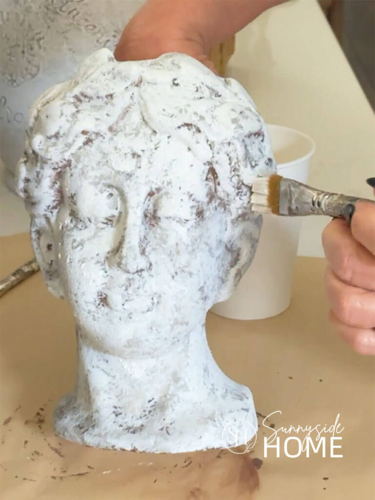 Woman pounces on white paint to add layers of texture and color to a ceramic head vase.