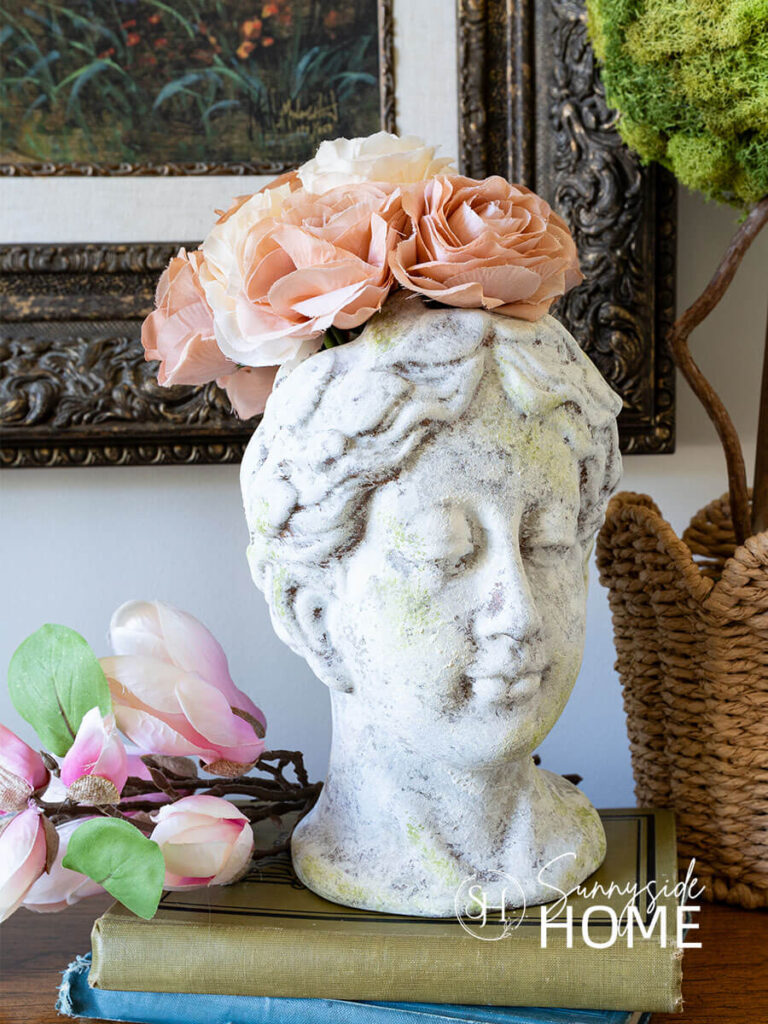 Old world texture finish on a vase styled with roses, on a book stack and a topiary.