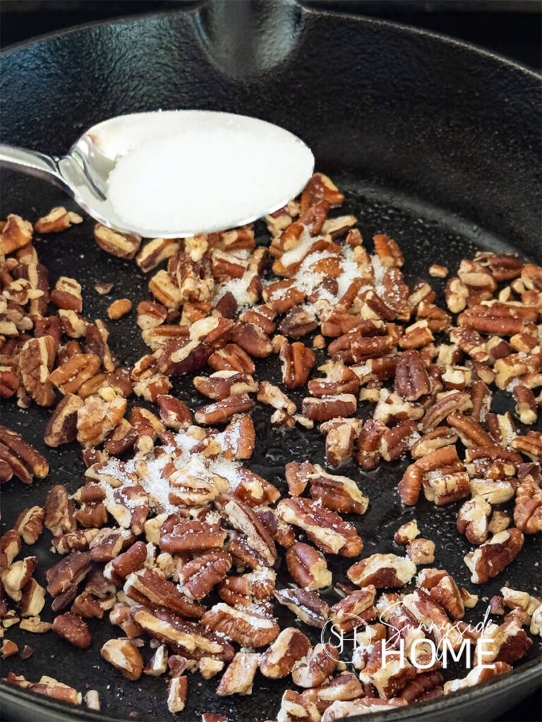 Pecans are toasted in a cast iron pan and sprinkled with monk fruit to caramelize them.