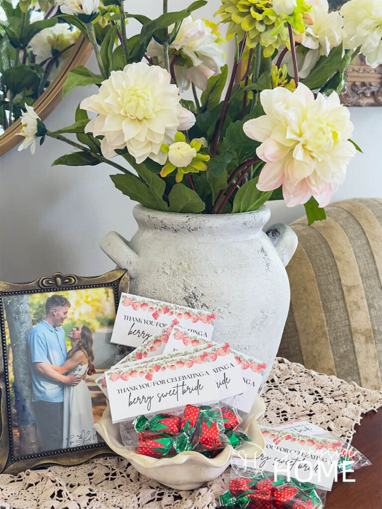 Strawberry candies in a cellophane bag with a label that reads: "Thank you for celebrate a berry sweet bride". styled with a photo of the bride and groom and a vase fille with zinnias and dalias.