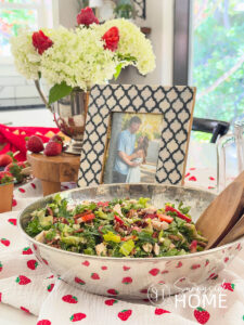 Bridal shower buffet with a strawberry table runner topped with a strawberry and chicken salad, photo of the bride and groom, floral arrangement with white hydrangeas and strawberries.