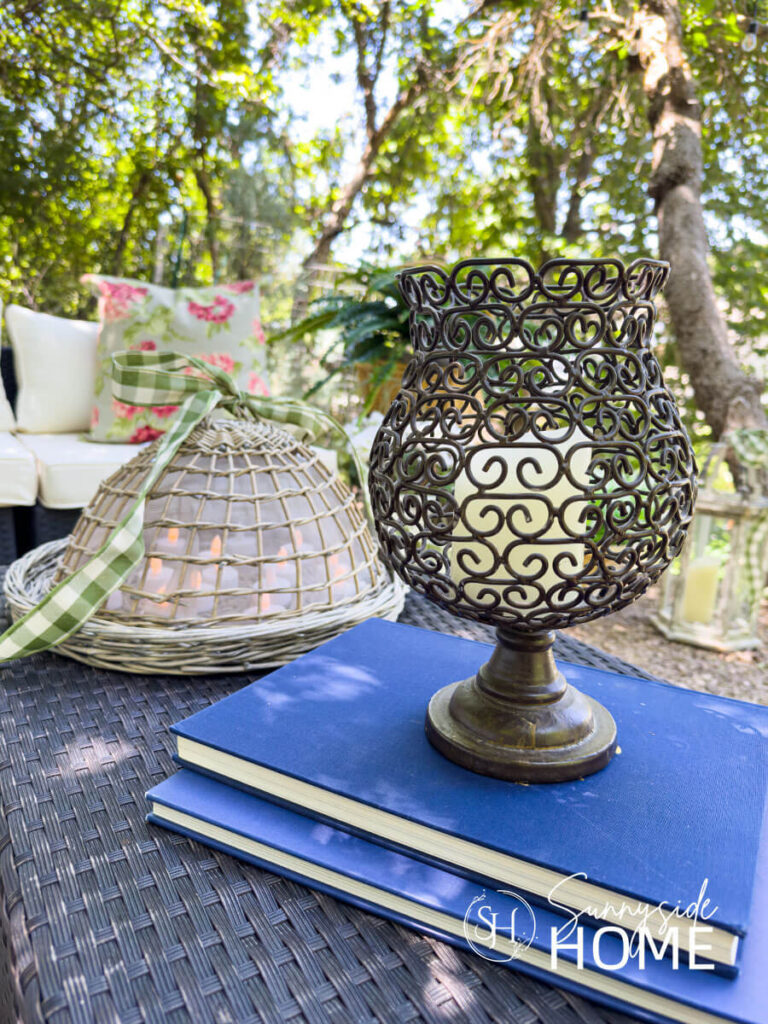 Outdoor coffee table styled with a basket dome with LED candles and embellished with a gingham ribbon, candle holder styled with books.