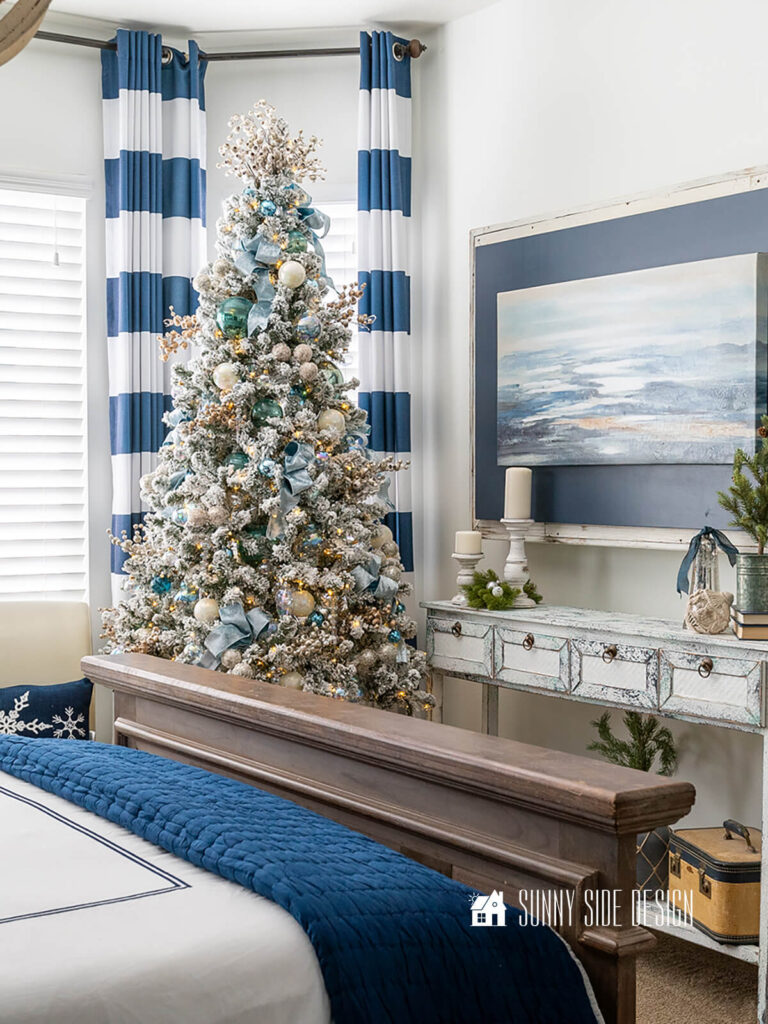 Blue and white decorated Christmas tree in a master bedroom with coastal art, blue and white stripe curtains.