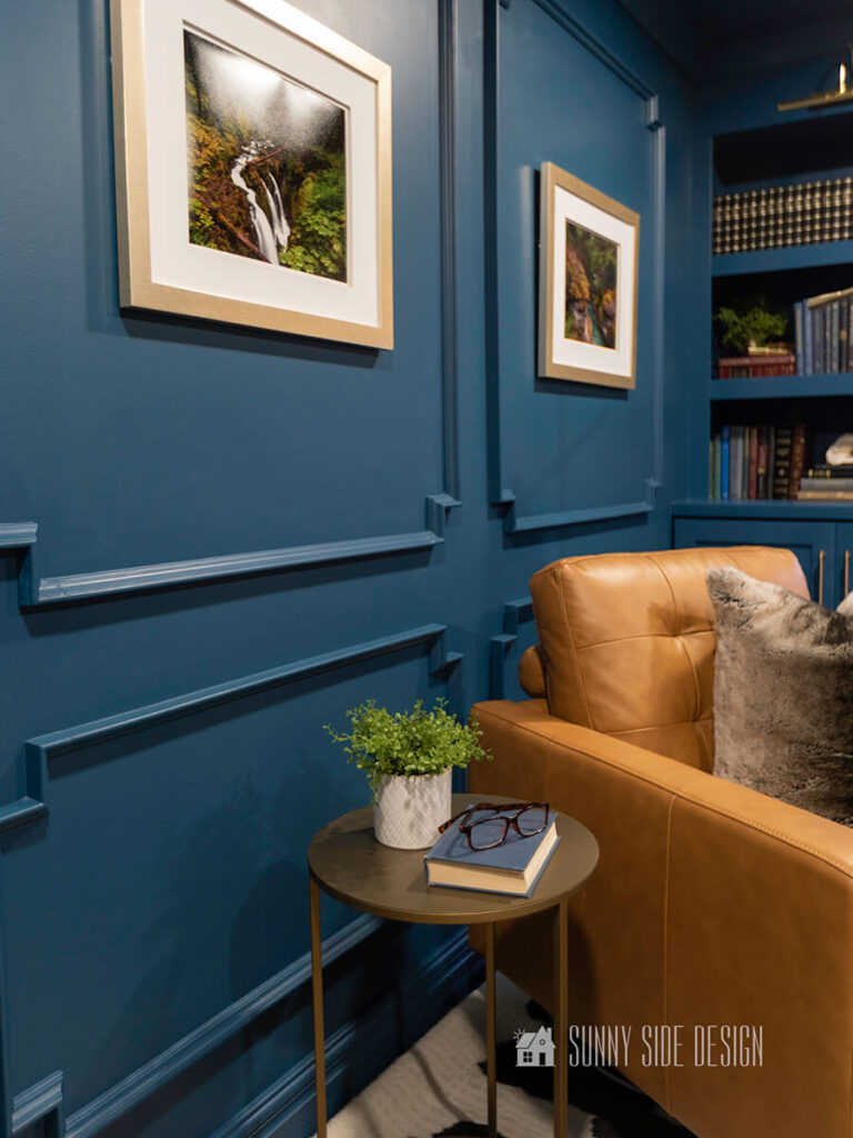 Home office and library, color drenched in a moody blue with white matted art on the walls and a leather reading chair.