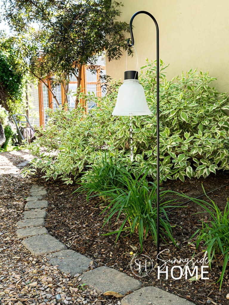 Repurpose glass lamp shades into garden pathway solar lights with chandelier crystals, hung from a black shepherds hook.