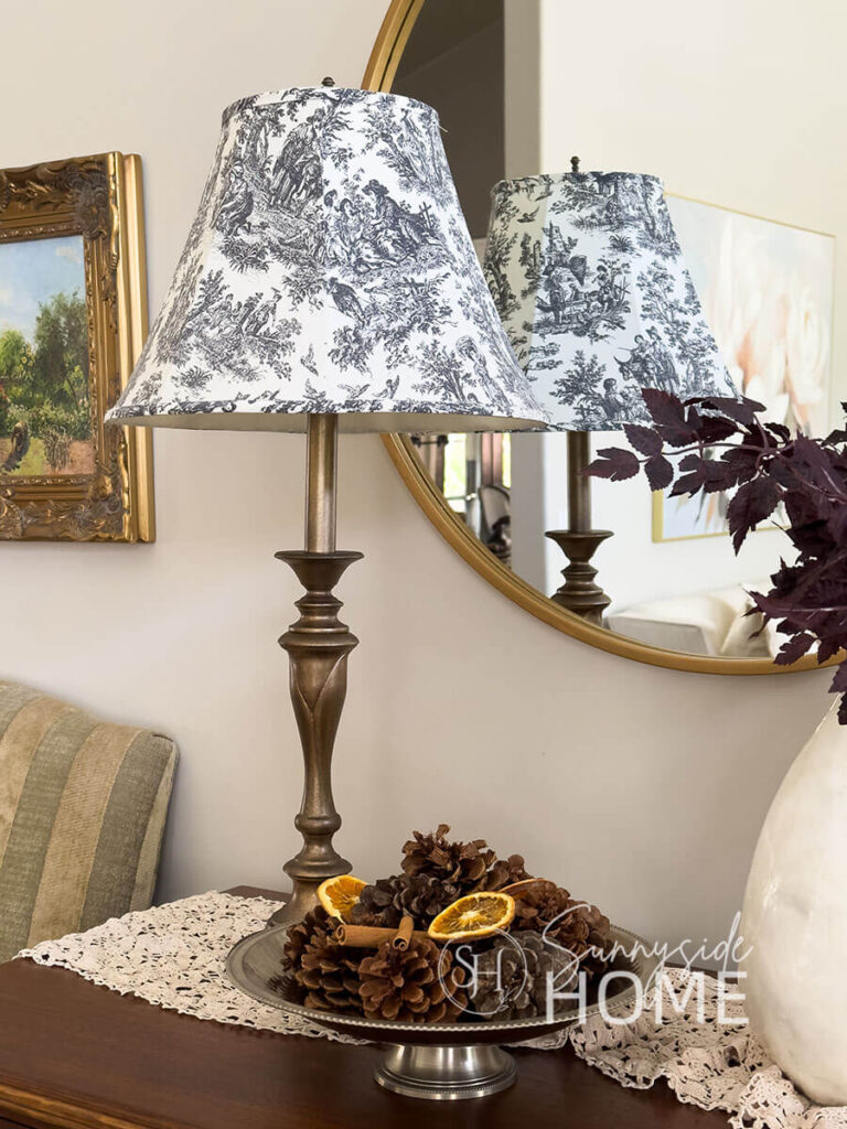 A thrifted lamp is given a make over with spray paint to give it an aged brass finish. Styled on a vintage dresser with scented pinecones, cinnamon sticks and dried orange slices on a vintage pedestal bowl.