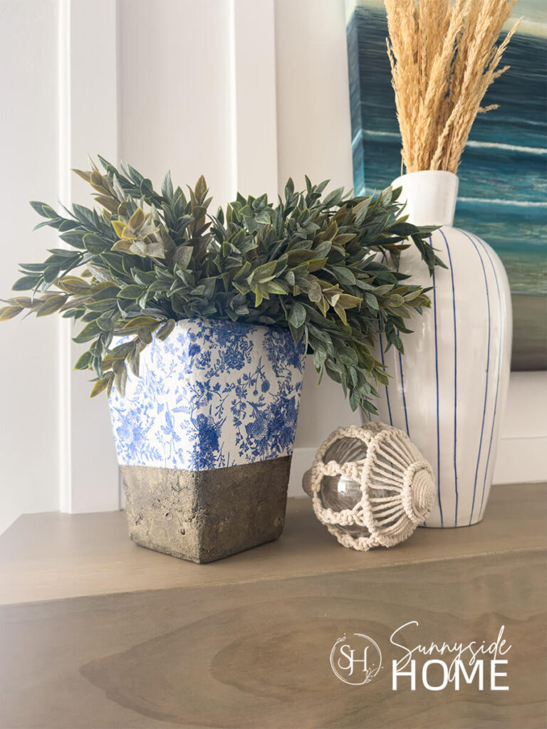 Blue and white decoupaged vase with napkins styled on a mantle with a blue and white stripe vase.