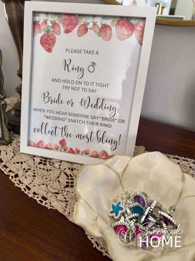 A framed graphic of a bridal shower ring game and a bowl filled with plastic rings.