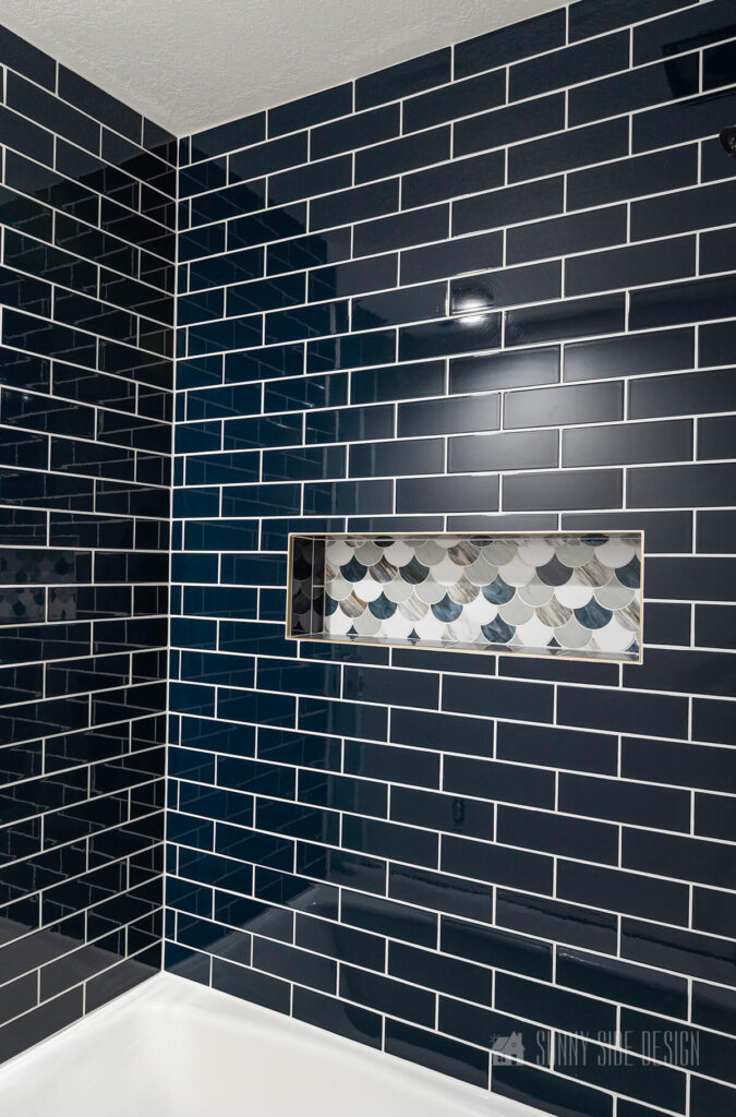 Scalloped tiles in various colors of blue in a shower niche with the remainder of the shower surround with a navy blue subway tile.