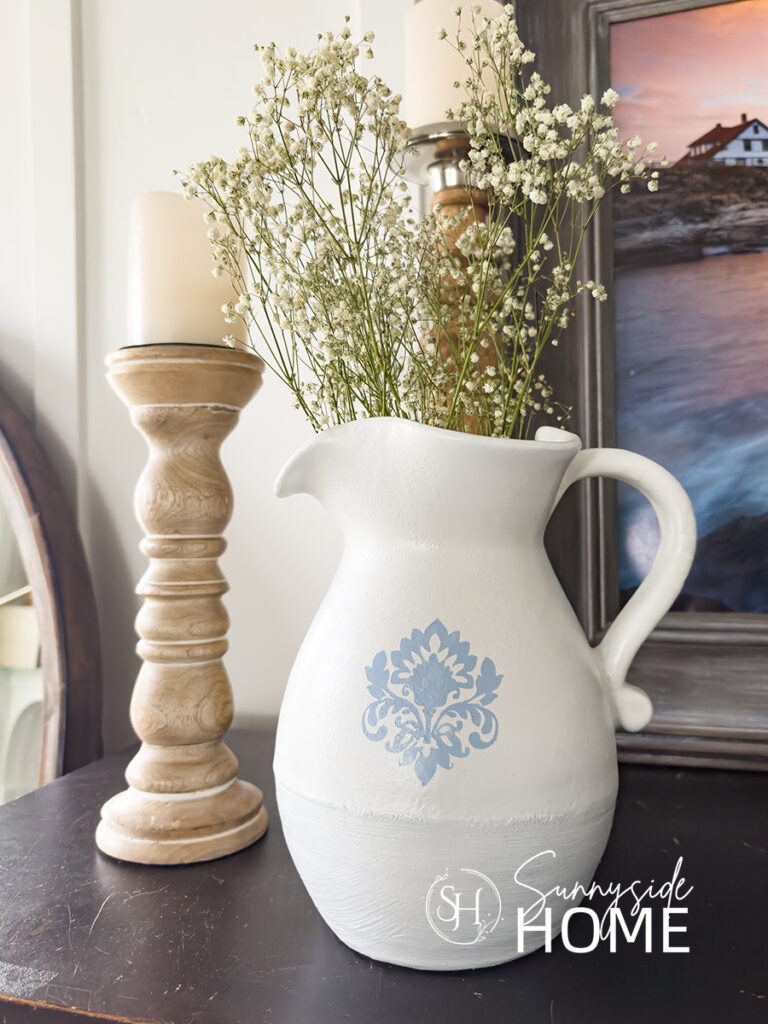 Old pitcher is given new life with white paint and a stenciled blue motif, styled with babies breath and candles.