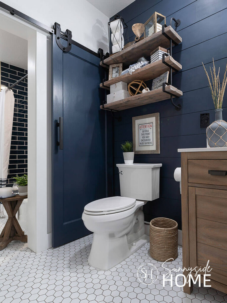 Decorate with blue and white in the bathroom with a navy barn door and white walls and white hexagon tile floor.