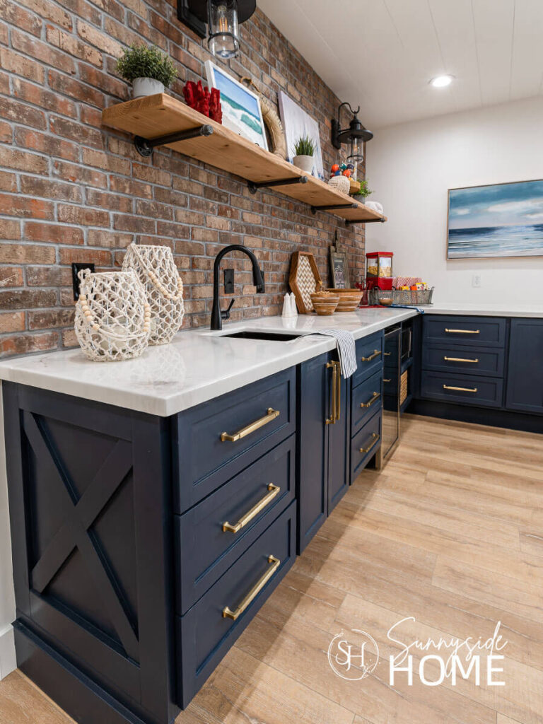 Paint cabinets blue, tope with a white marble counter with a rustic brick backsplash. Pretty gold drawer pulls embellish the blue cabinets and is an easy way to decorate with blue and white.