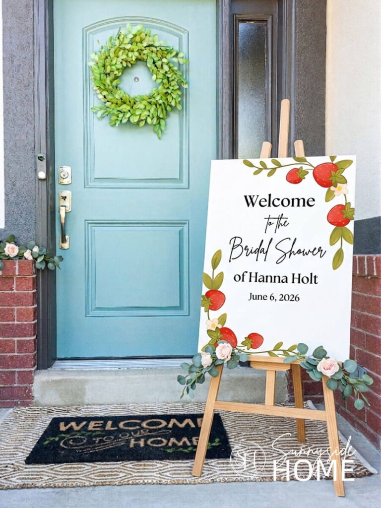 Bridal Shower Welcome sign on a front porch with a blue front door and a boxwood wreath.