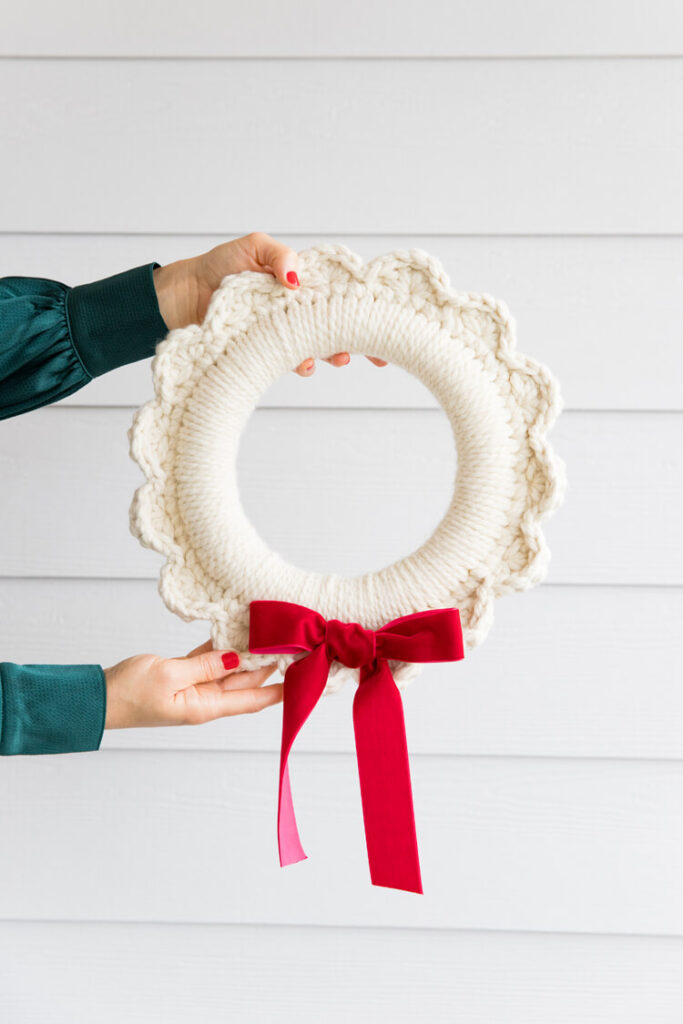 Woman holds a crocheted yarn scalloped wreath with a red velvet bow.