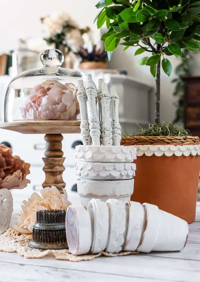 Clay pots are embellished with clay scallops and painted white, styled with topiary tree, cloche with flower and white painted spindles.