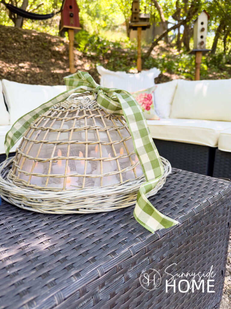 Outdoor coffee table styled with a basket dome with LED candles and embellished with a gingham ribbon.