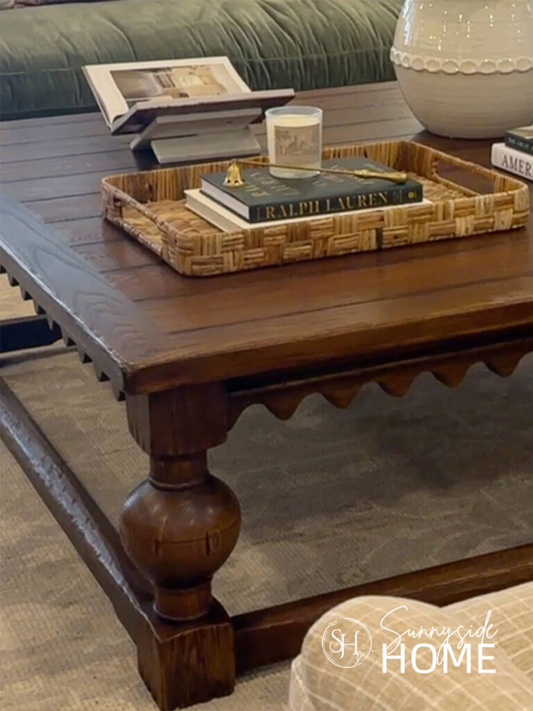 A dark stained coffee table with a pretty scalloped border, styled with a tray with decor books, candle and snuffer.