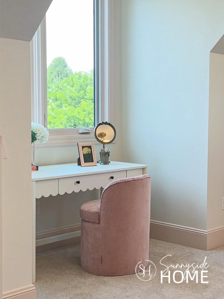 A white scalloped edge desk in a bedroom nook with a pink velvet chair.