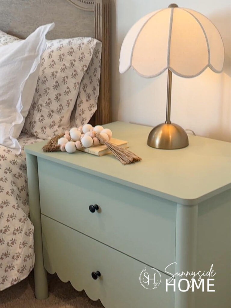 A brass lam with a scalloped shade styled on a green scalloped nightstand in a little girls bedroom.