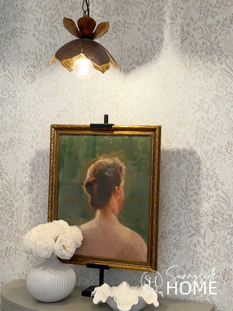 A pretty scalloped pendant light hung over a half round cabinet, styled with art, vase of white flowers and a scalloped bowl.