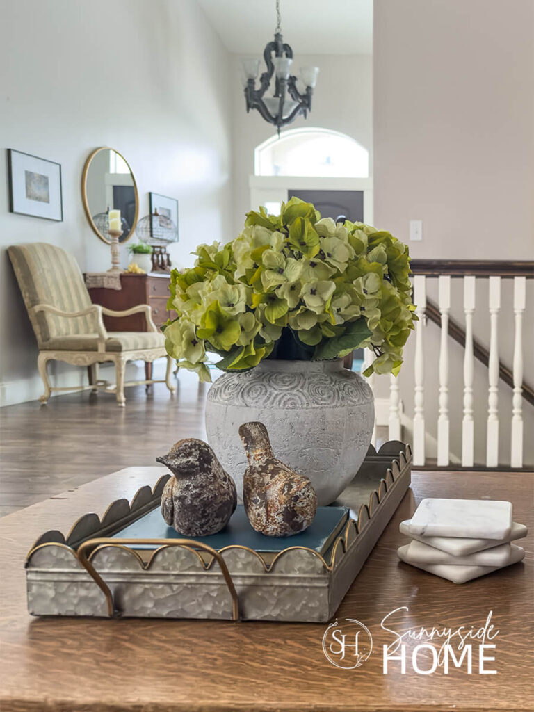 A galvanized scalloped tray on a oak coffee table styled with a vase of green hydrangeas, book stack and bird decor.
