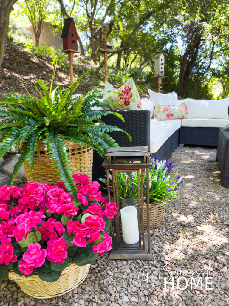 Outdoor living space with potted ferns and flowers, lanterns styled by an outdoor sectional with floral pillows.