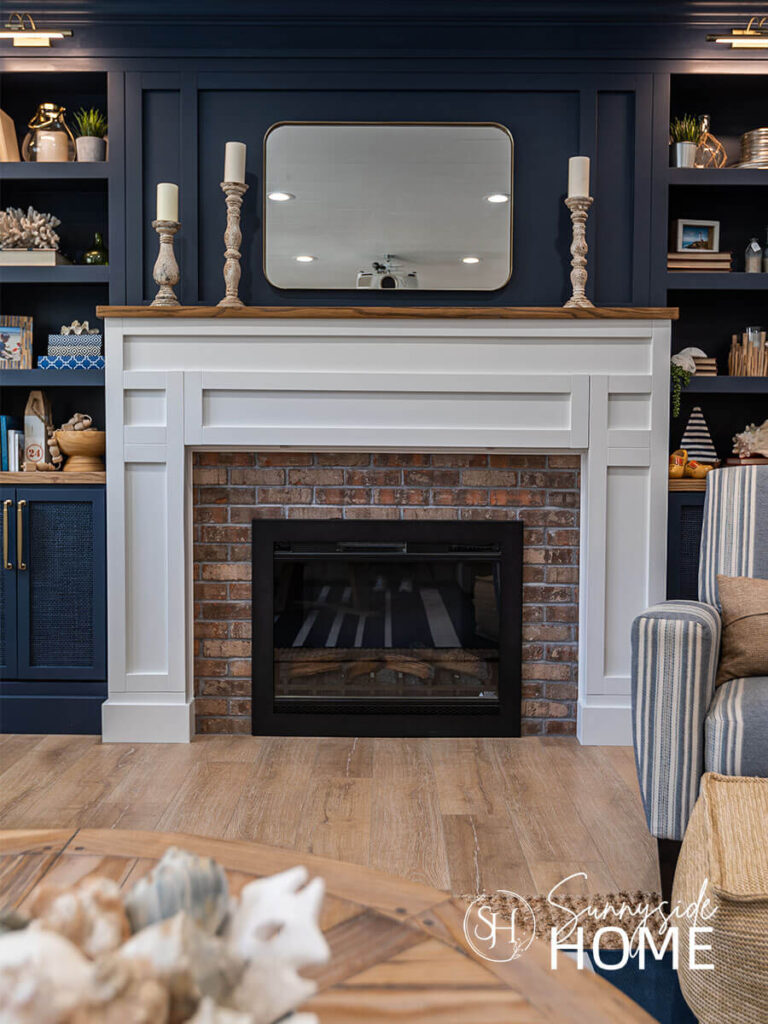 Over mantle and built-in bookshelves painted blue with the mantle surround painted white in a basement family room with assorted coastal and vintage decor.