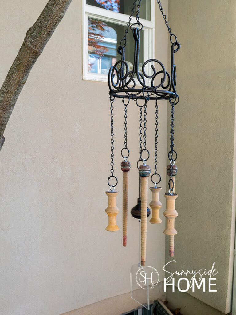 Charming wind chime hung from a maple tree made with an inverted plant stand, vintage spools and door knob.