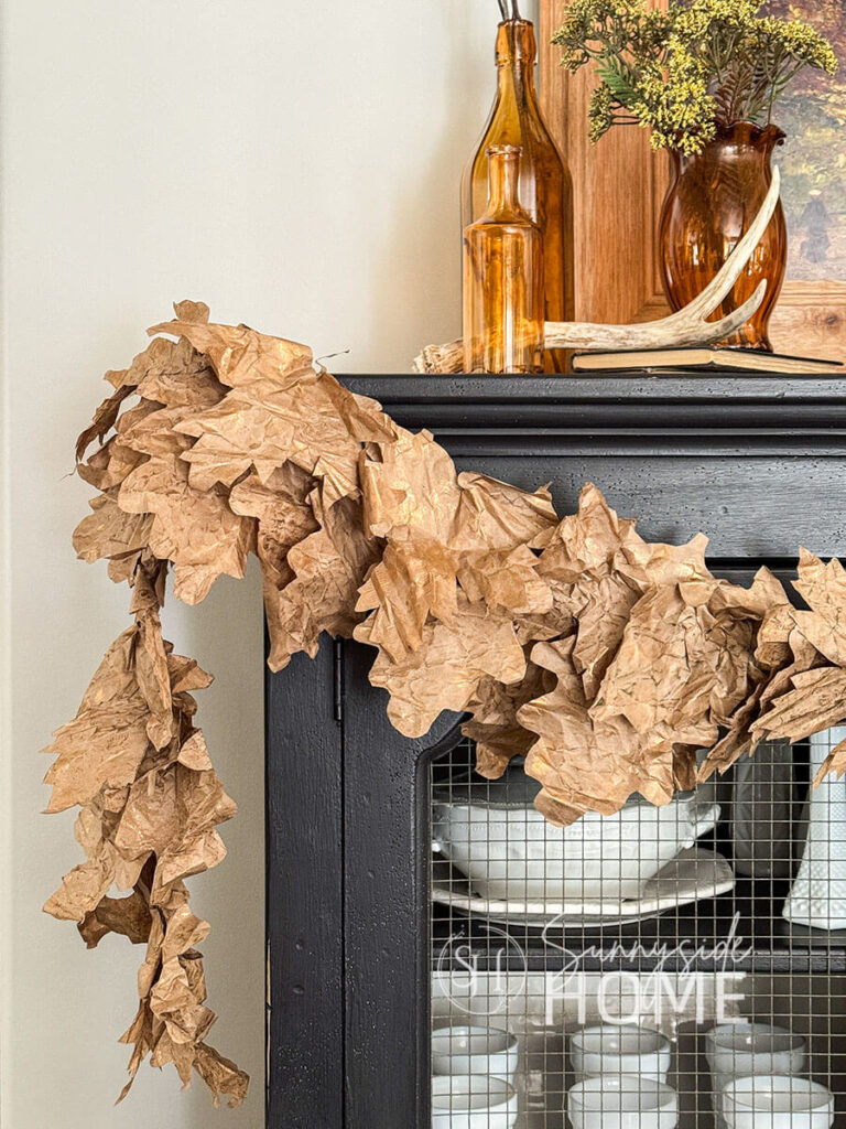 A simple fall leaf garland swaged across a black china cabinets, made with recycles packaging paper.