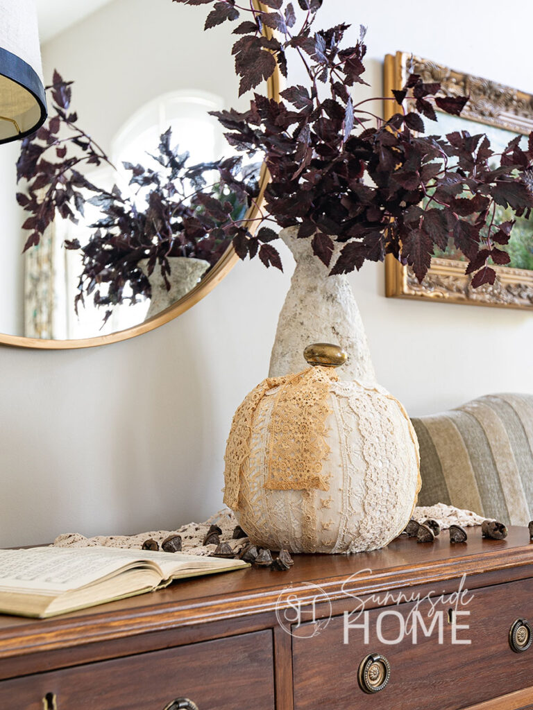 A simple DIY fall decor pumpkin made with vintage lace and brass door know for the stem. Styled with a vase of burgundy leaves and scattered eucalyptus pods.