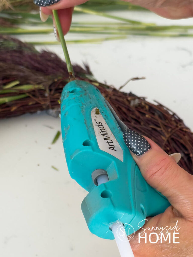 Woman applies hot glue to a pampas grass stem.