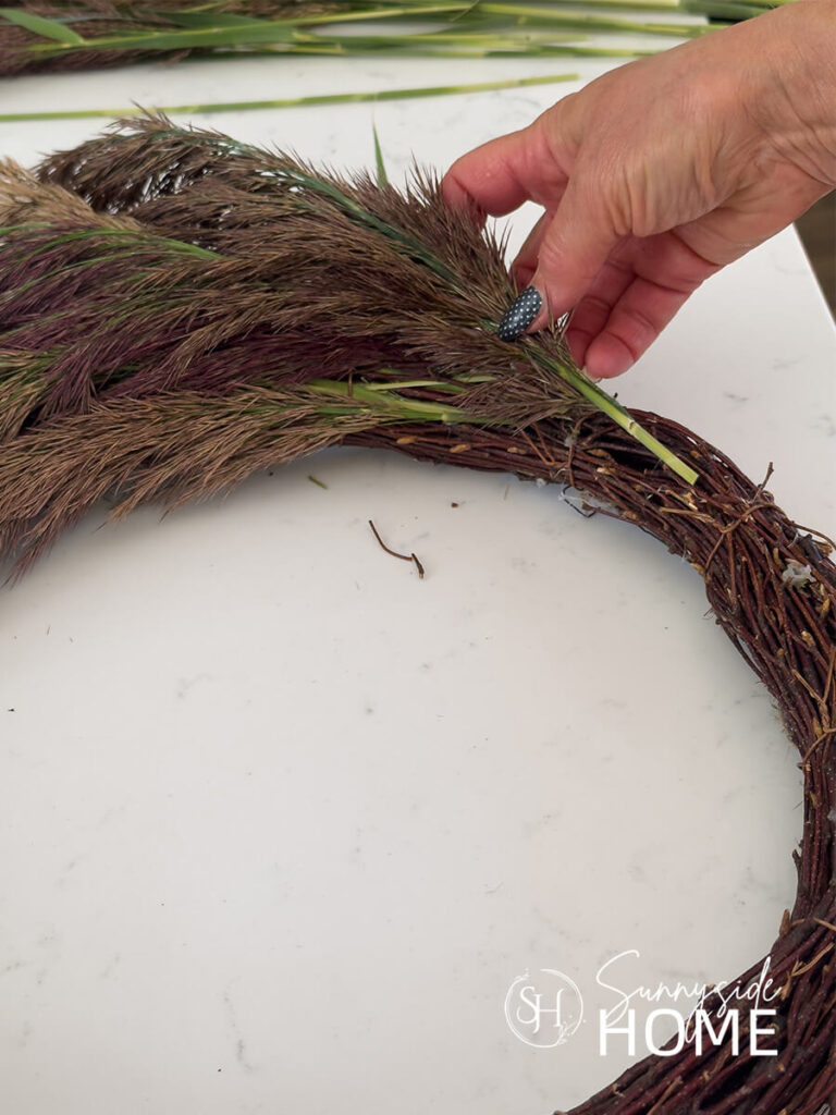 Woman inserts a pampas grass stem into a grapevine wreath.