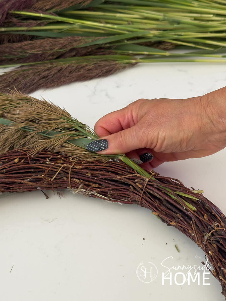 Woman inserts a pampas grass stem into a grapevine wreath.