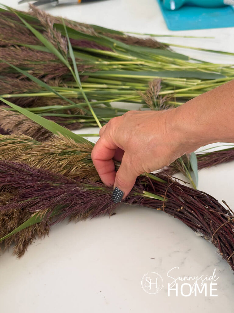 Woman inserts a pampas grass stem into a grapevine wreath.