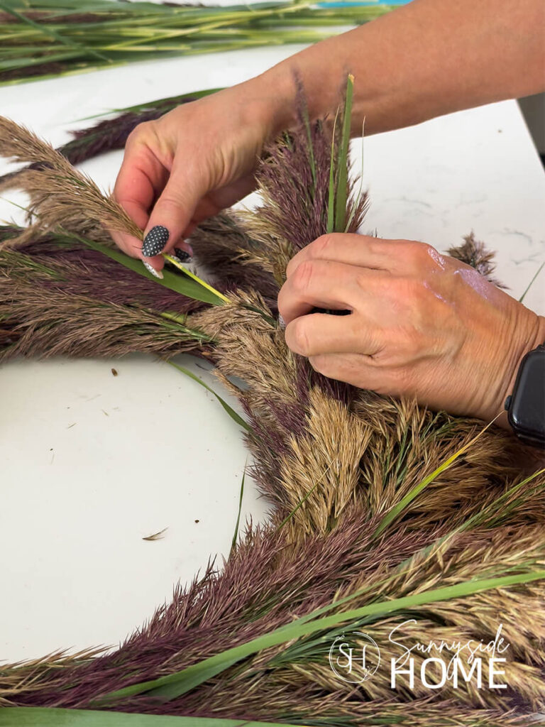 Woman inserts the final pampas grass stem into the wreath.
