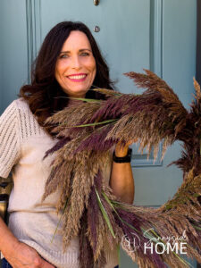 Woman holds Beautiful Pampas Grass Wreath for Fall by a blue front door.