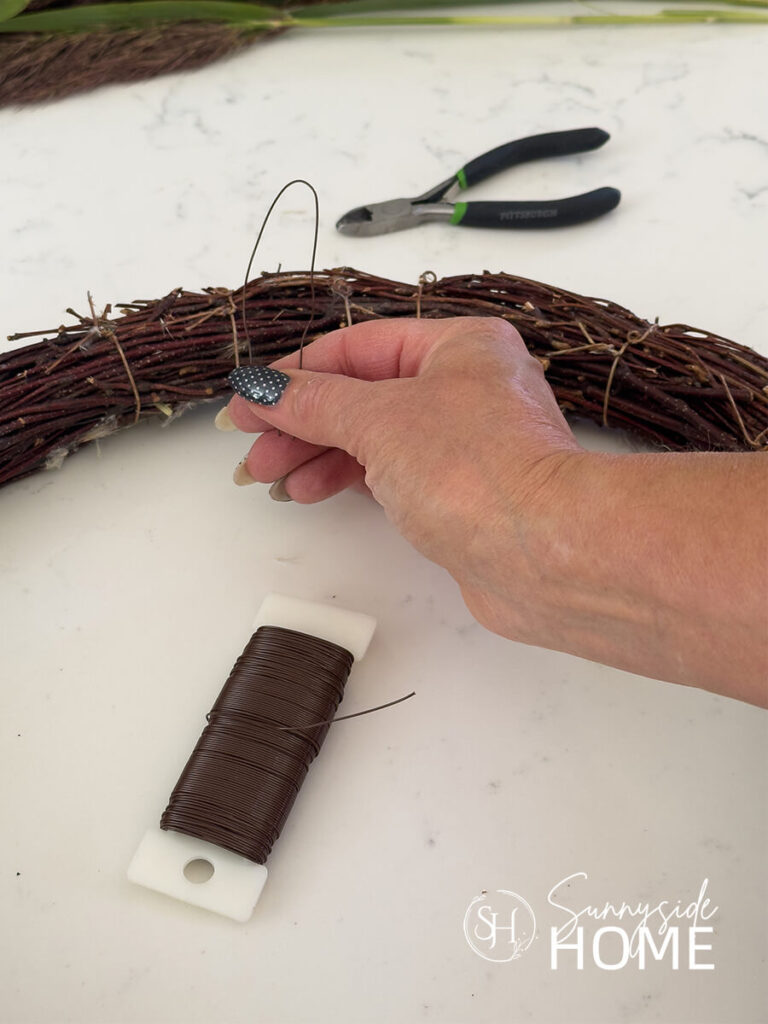 Woman holds a loop of wire to create a hanger for a grapevine wreath.