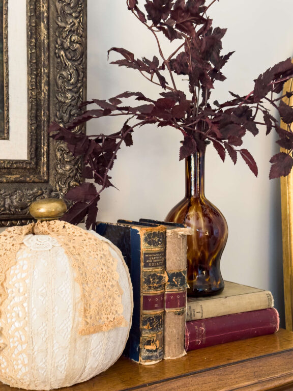 Classic fall decorating trends with vintage books, tortoise shell vintage vase with burgundy stems and a vintage lace pumpkin.